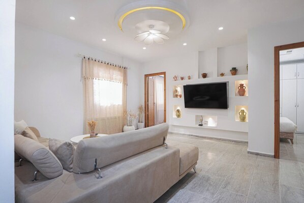 A modern living room with a sofa, television, decorative items, and a door leading to another room. - Charming 3-Bedroom Apartment in Historic Carthage, Tunisia (Site archéologique de Carthage)