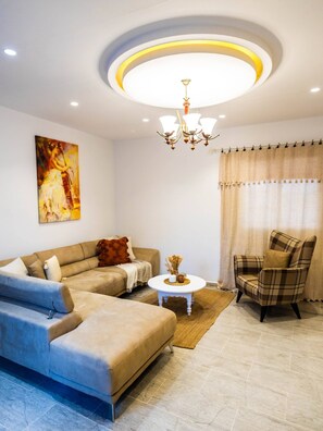 A living room with a sectional sofa, a plaid armchair, a coffee table, and a chandelier. - Charming 3-Bedroom Apartment in Historic Carthage, Tunisia (Site archéologique de Carthage)