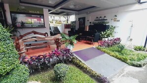 Un espace d’accueil avec un banc, des plantes en pot et un petit coin salon extérieur.