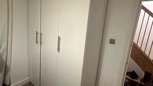 A room with a large white wardrobe, a door leading to a staircase, and a carpeted floor. - Charming 1-Bedroom Apartment in Central London (London)