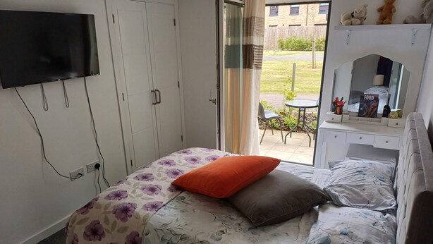 A bedroom with a bed, a TV mounted on the wall, a window with a view of the outside, and a small table with a lamp. - Holiday home with private bathroom (Edinburgh)