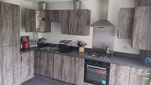 A modern kitchen with wooden cabinets, a stainless steel stove, and a built-in oven. - Holiday home with private bathroom (Edinburgh)