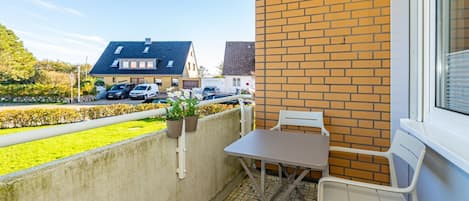 Un balcon avec une table et des chaises, des plantes en pot et une vue sur une rue bordée de voitures garées et de maisons.