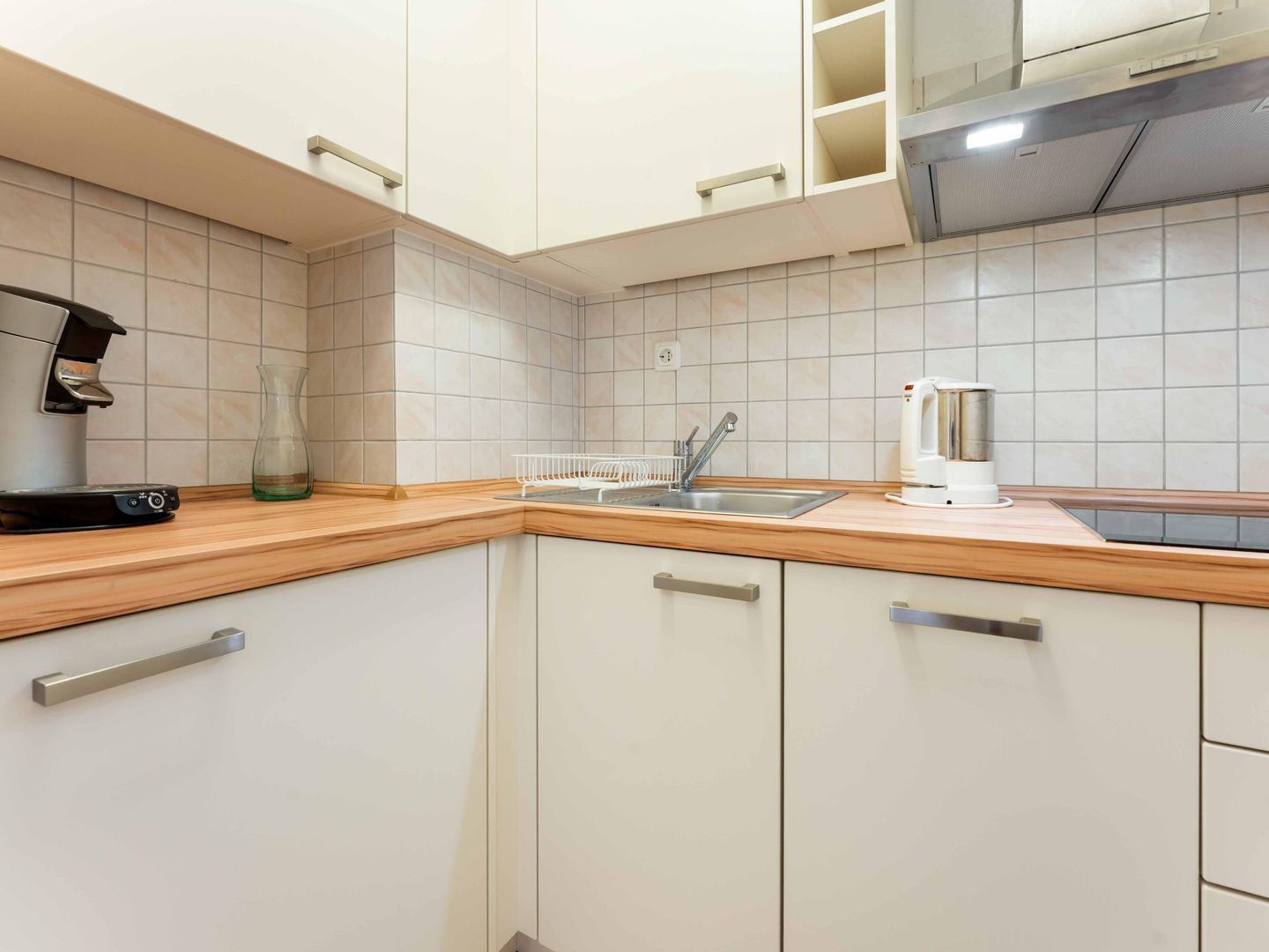 A kitchen with white cabinets, a wooden countertop, a coffee maker, and a kettle.