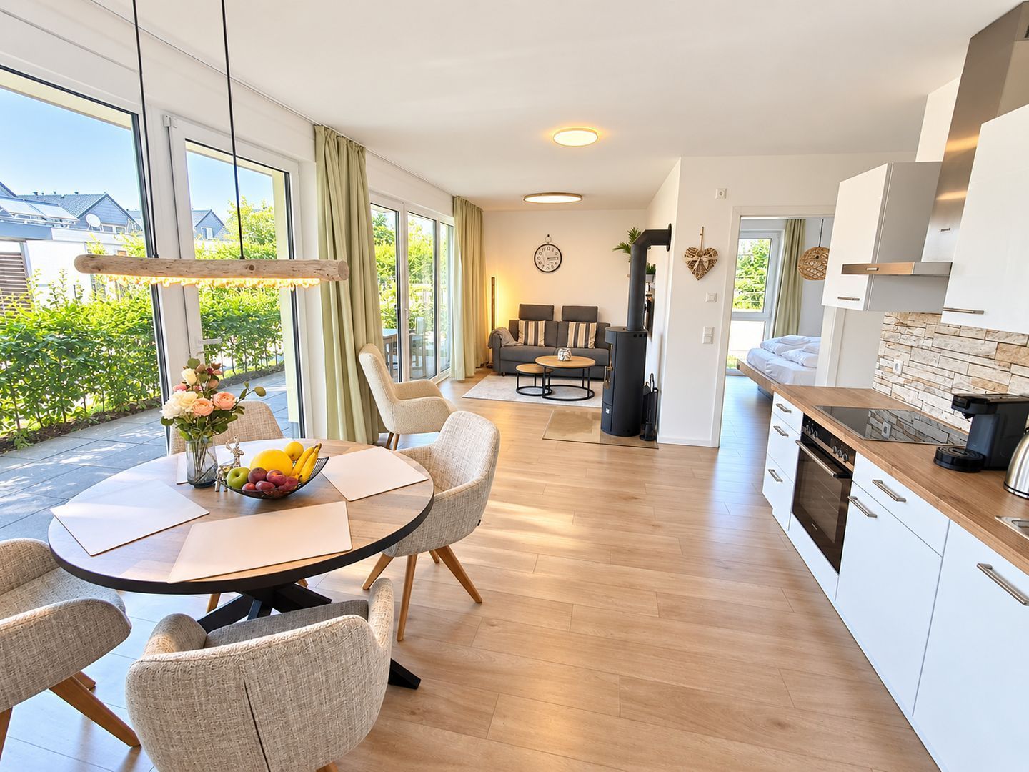 Cozinha moderna com ilha central, área de jantar com mesa redonda e sala de estar com sofá e cadeiras.