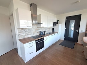 Eine moderne Küche mit weißen Schränken, einer Küchenrückwand aus Stein und einem schwarzen Backofen.