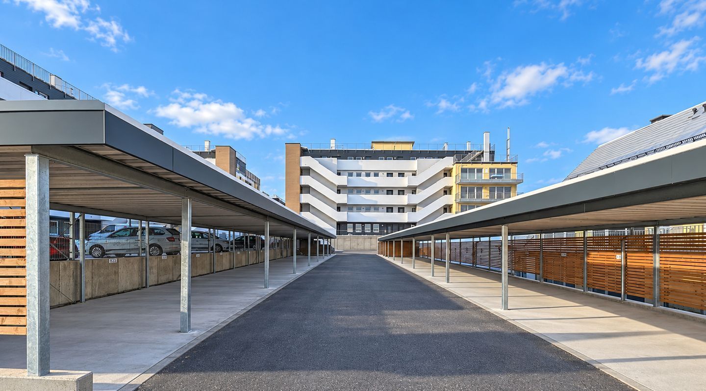 A covered parking area with multiple levels of parking, a central walkway, and a building in the background.