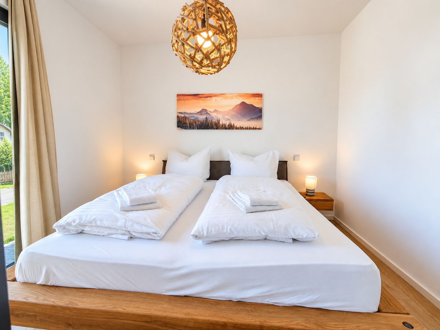 A double bed with white linens, a wooden headboard, a wall-mounted picture, and a hanging light fixture.
