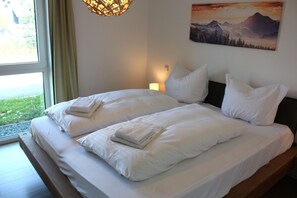 Ein Doppelbett mit weißer Bettwäsche, eine Nachttischlampe und ein Gemälde mit Berglandschaft an der Wand.
