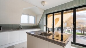 A modern kitchen with a large island, a window, and a sliding glass door leading to an outdoor area. - Hotel Harbor (Tongyeong)