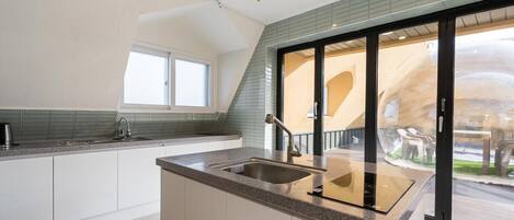 A modern kitchen with a large island, a window, and a sliding glass door leading to an outdoor area.
