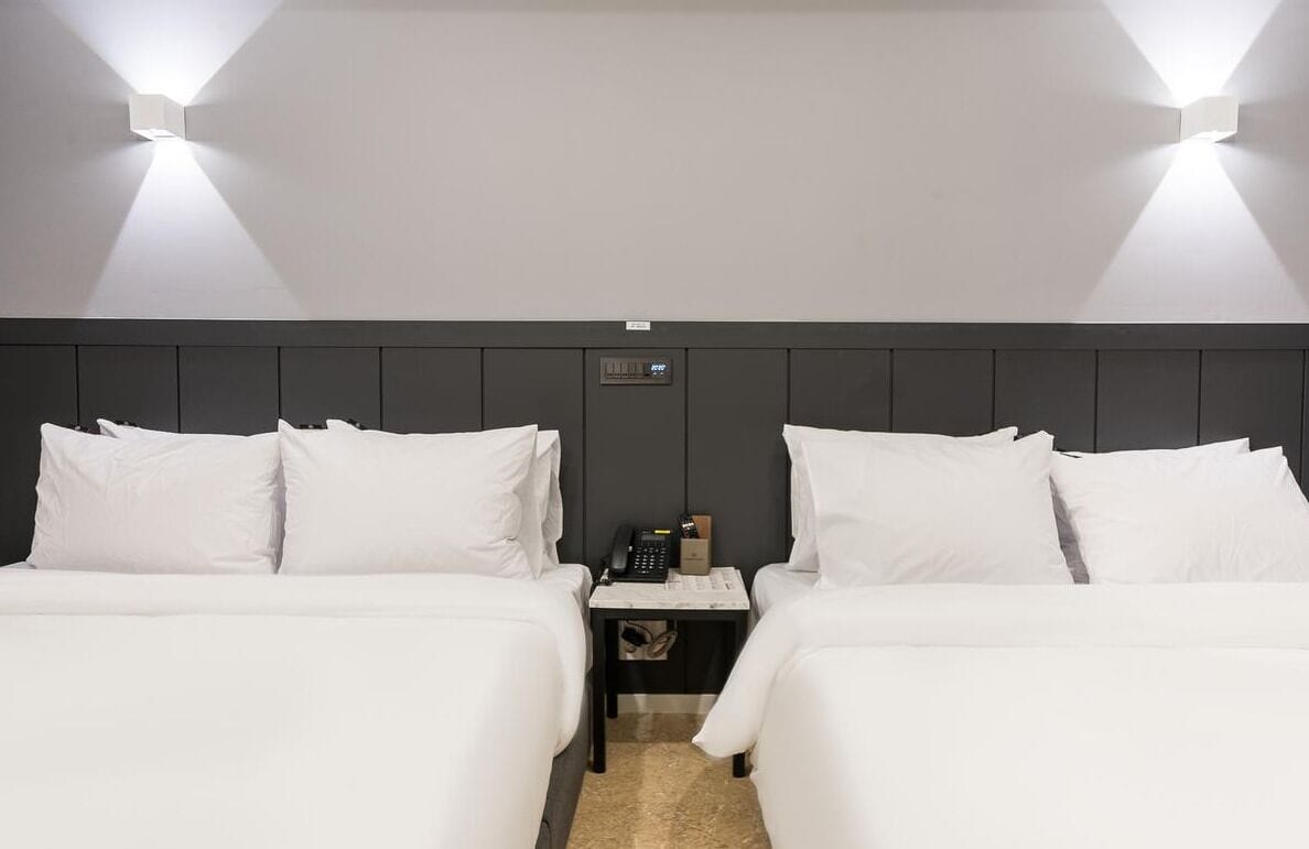 A hotel room with two beds, a nightstand, and a wall-mounted phone.