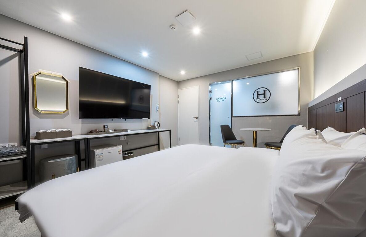 Egy modern szállodai szoba, melyben található egy nagy ágy, egy íróasztal, egy síkképernyős televízió, egy ülősarok és egy minibar.