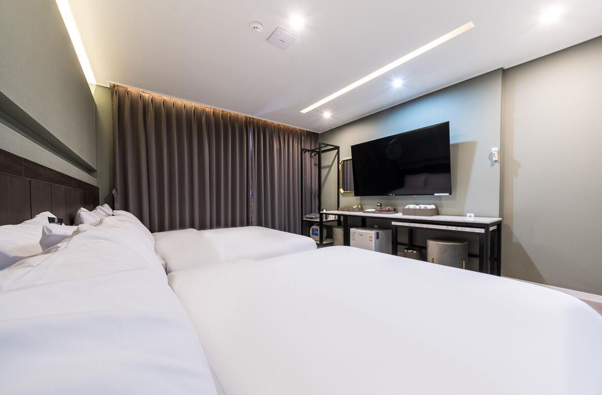 A hotel room with a large bed, a desk with a flat-screen TV, and a curtain.