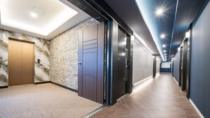 A modern hallway with a marble wall, a wooden door, and a blue ceiling. - Hotel Harbor (Tongyeong)