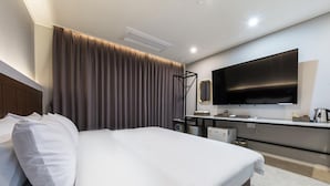 A modern hotel room with a large bed, a flat-screen TV mounted on the wall, a desk with a chair, and a window with curtains. - Hotel Harbor (Tongyeong)