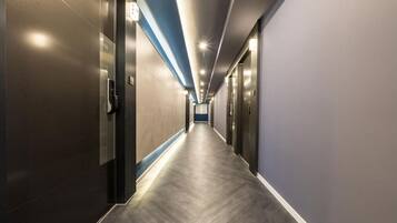 A modern hotel corridor with a long, straight path, doors on both sides, and a ceiling with recessed lighting.