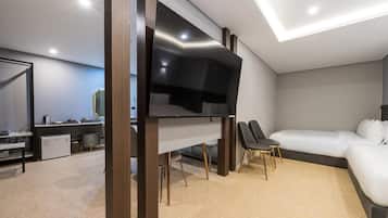 A modern bedroom with a flat-screen TV, a sofa, and a dining area with a refrigerator and a kettle.