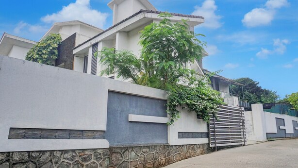 Une maison moderne avec des fondations en pierre, une façade blanche et un portail en métal.