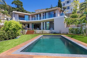 Een modern huis met twee verdiepingen, een zwembad, een overdekt terras en een verzorgde tuin.