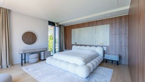 Quarto moderno com uma cama grande, um espelho redondo e vista para o verde lá fora.