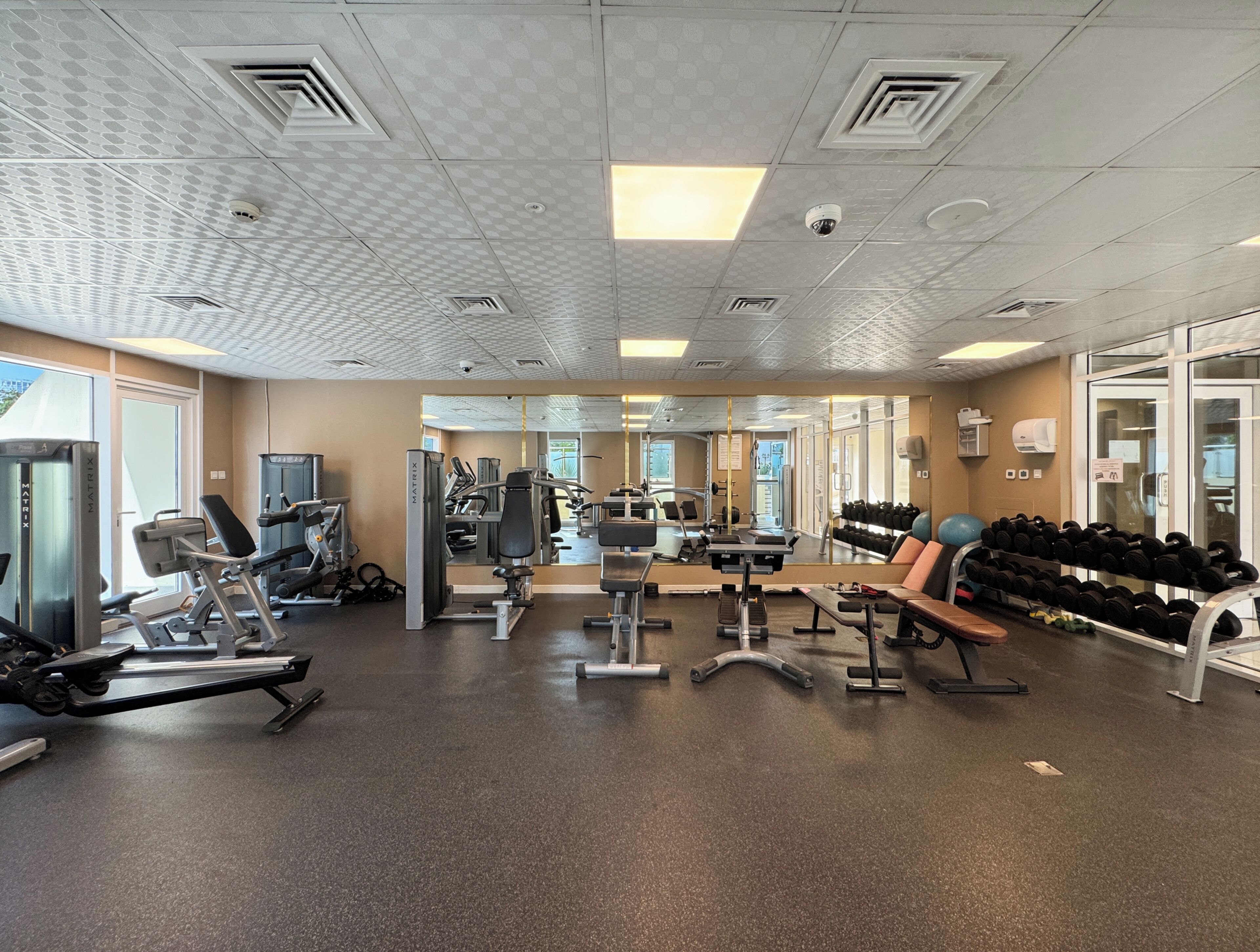 Un gimnasio con equipo de ejercicio variado, incluyendo cintas de correr, máquinas de pesas y mancuernas.