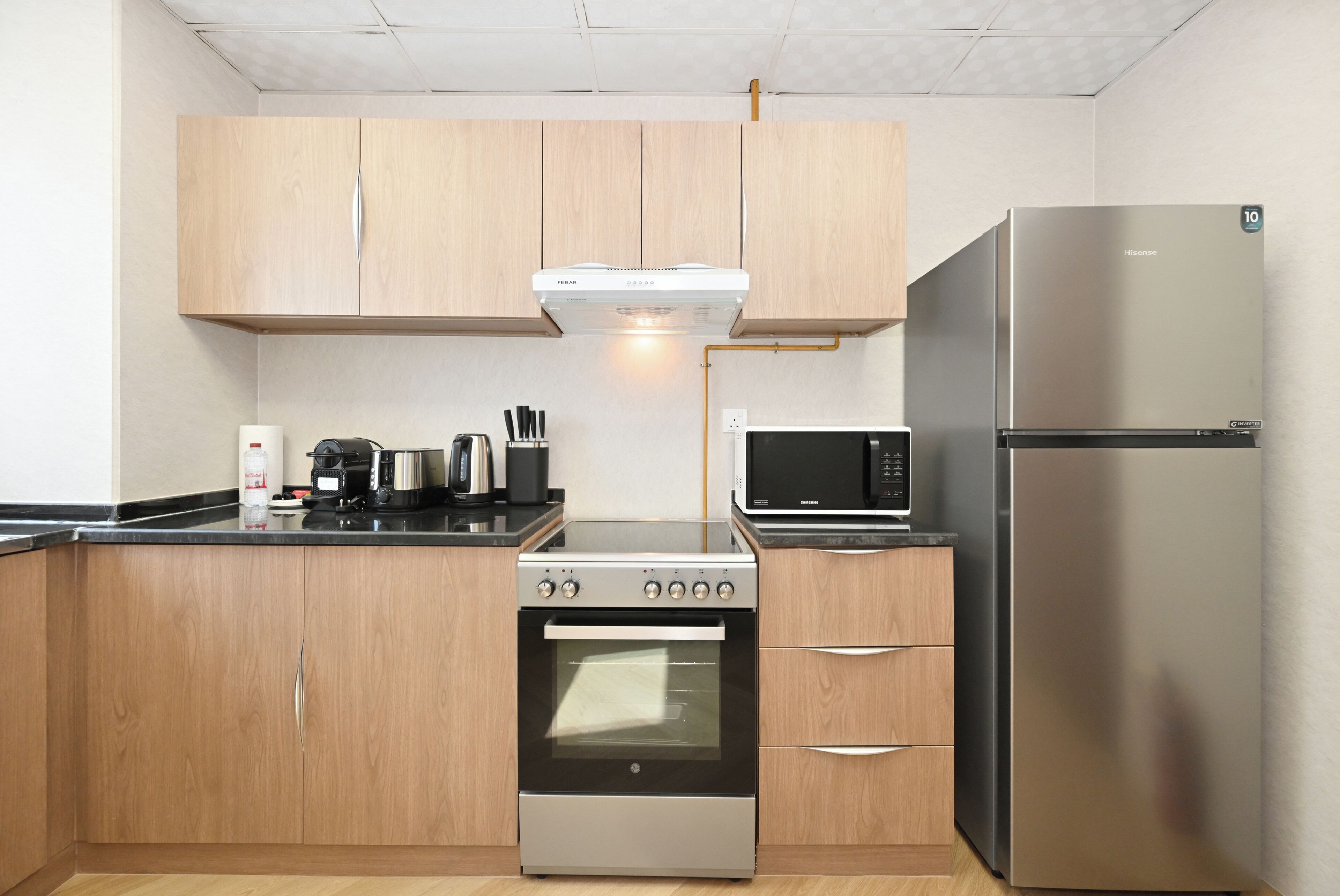 Een compacte keuken met houten kastjes, een roestvrijstalen koelkast, een magnetron, een fornuis en een koffiezetapparaat.