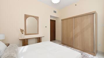 Un dormitorio con cama, mesita de noche, espejo, armario y puerta que da a otra habitación.