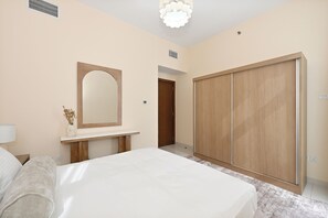 Un dormitori amb un llit, una tauleta de nit, un mirall, un armari i una porta que dona a una altra habitació.