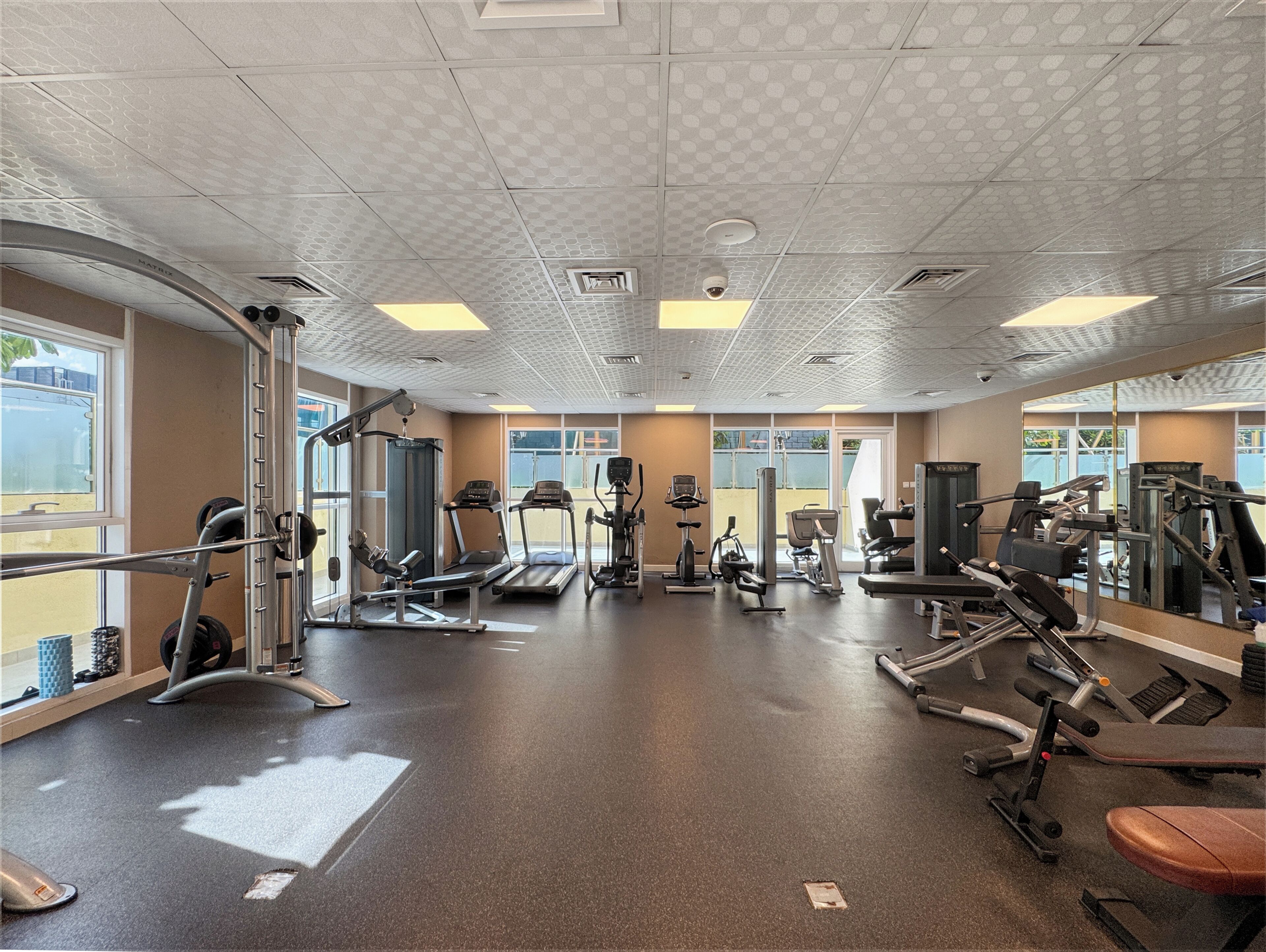 A gym with various exercise equipment, large windows, and a patterned ceiling.