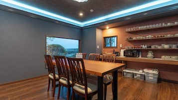 A dining area with a wooden table and chairs, a view of the outdoors, and shelves with kitchenware.