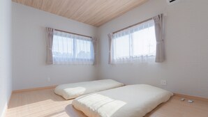 A room with two beds, a sloped ceiling, and large windows with curtains.