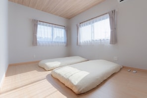 A room with two beds, a sloped ceiling, and large windows with curtains.