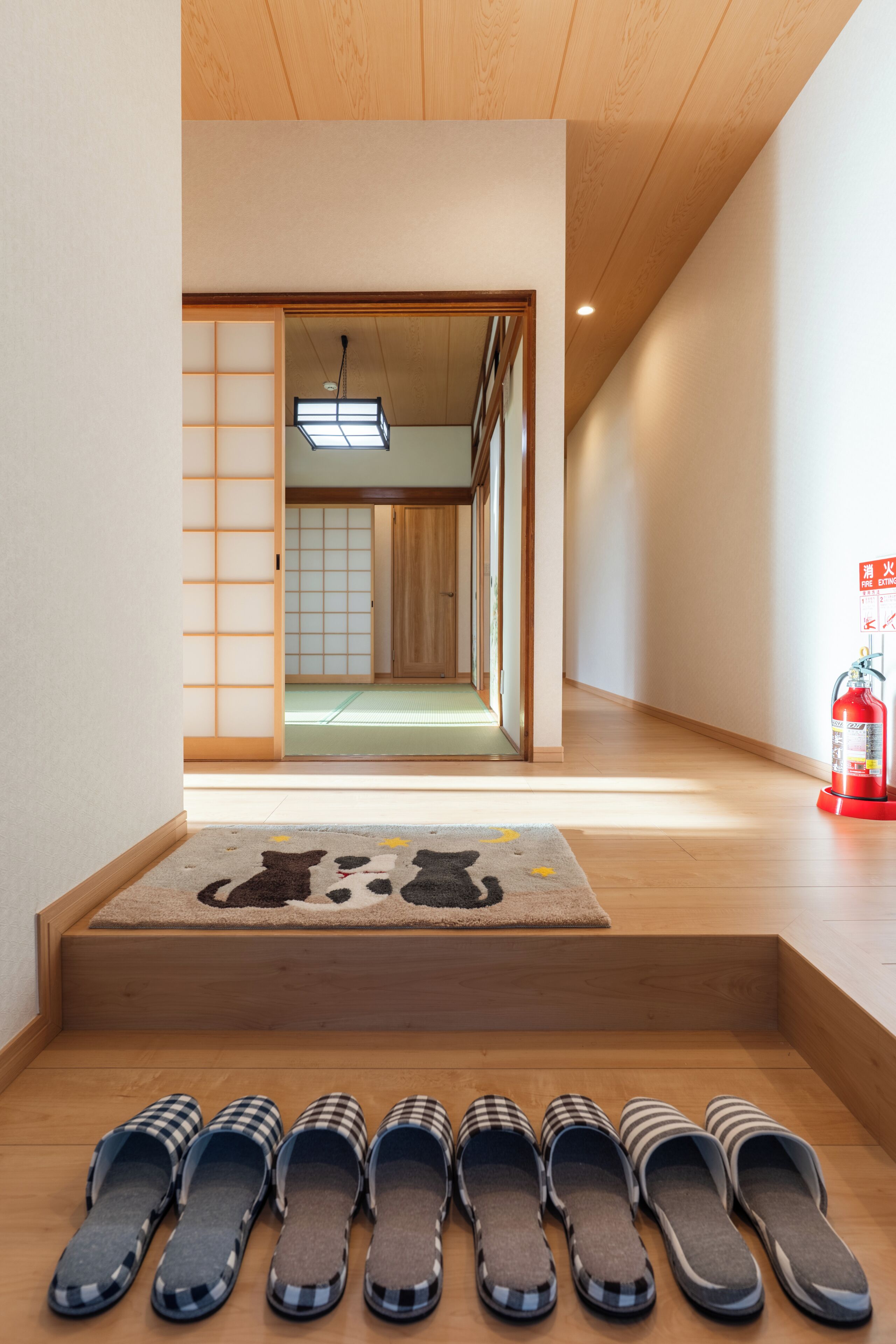 Een hal met een houten vloer, een ingang met tatami matten en een brandblusser aan de rechterkant.
