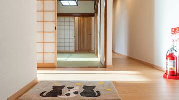 Een hal met een houten vloer, een ingang met tatami matten en een brandblusser aan de rechterkant.