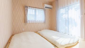 A room with two beds, a window with curtains, and an air conditioning unit.