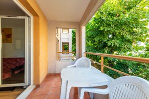 A balcony with a white table and chairs, a wooden railing, and a view of green foliage. - Apartment with balcony and swimming pool, sleeps 4 (Grasse)