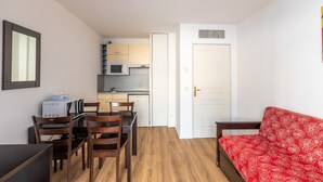 Un espacio habitable compacto con comedor, kitchenette y un sofá rojo estampado.