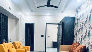 Una sala de estar moderna con un sofá, dos sillones, un ventilador de techo y piso de mármol.