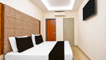 A hotel room with a bed, a flat-screen TV, an air conditioning unit, and a door.