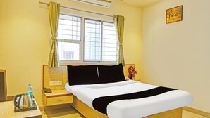 A hotel room with a bed, a bedside table with a phone and a water bottle, a window with curtains, and a painting on the wall. - Super Collection O Pune Nagar Road Viman (Pune)