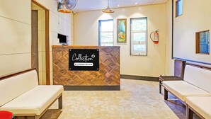 A reception area with a 'Collection' sign, a reception desk, two benches, a wall-mounted fan, and a fire extinguisher. - Super Collection O Pune Nagar Road Viman (Pune)