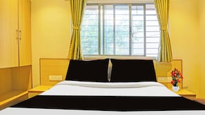 A hotel room with a bed, a nightstand, a window with curtains, and a wall-mounted light switch. - Super Collection O Pune Nagar Road Viman (Pune)