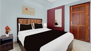 A bedroom with a large bed, a wooden wardrobe, a nightstand, and a wall-mounted mirror. - Super Collection O Valiyavila Junction (Thiruvananthapuram)