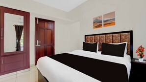 A hotel room with a large bed, a wardrobe, a nightstand with a vase of flowers, and two landscape paintings on the wall. - Super Collection O Valiyavila Junction (Thiruvananthapuram)