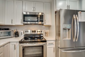 Eine moderne Küche mit weißen Schränken, einem Edelstahl-Kühlschrank, einem eingebauten Backofen, einer Mikrowelle und einem Toaster.