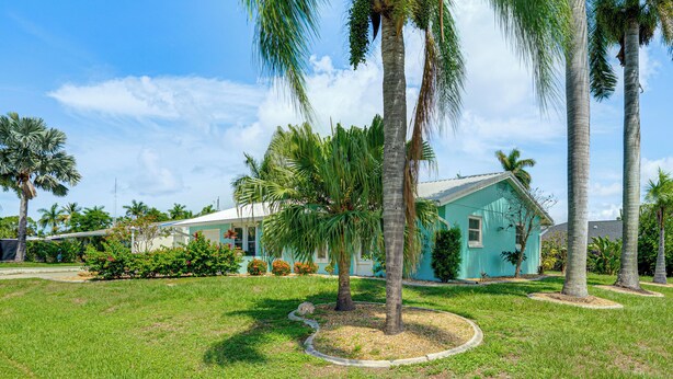 Une propriété résidentielle dotée d’une pelouse bien entretenue, de palmiers et d’une maison aux murs turquoise.