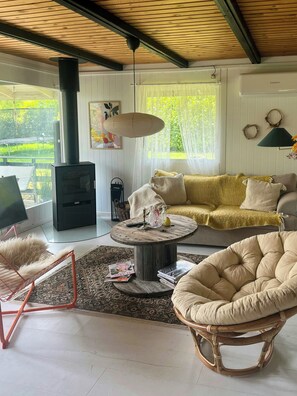 Una sala de estar acogedora con un sofá, una mesita redonda, un sillón de mimbre, una chimenea y vistas al exterior.