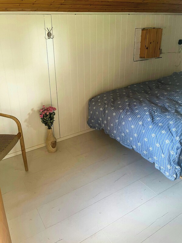 A bedroom with a bed, a chair, a wooden cabinet, and a vase with flowers.