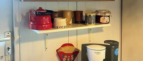 A kitchen with a coffee maker, kettle, and shelves with various kitchenware.